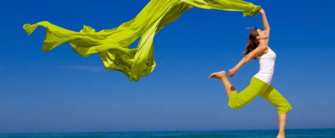 Beautiful young woman jumping on the beach with a colored tissue