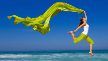 Beautiful young woman jumping on the beach with a colored tissue